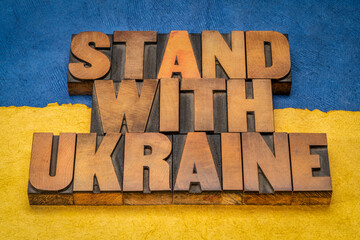 stand with Ukraine - words in vintage letterpress wood type against blue and yellow paper background in colors of Ukrainian national flag, help and support concept