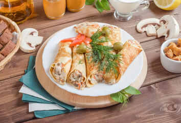Stuffed pancakes stuffed with cheese and champignons decorated with herbs on a white plate on a wooden background