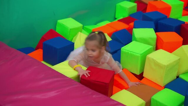 Little baby girl playing with soft cubes dry pool game children's room for birthday Entertainment centre Indoor playground foam rubber pit trampoline Caucasian female child dressed pink dress 