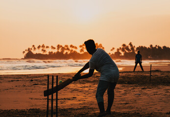 boy playing cricket at sunset on tropical beach in Sri Lanka