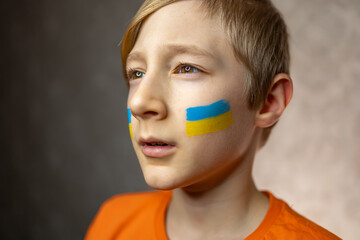 a child against war, a portrait of a boy with a painted flag of Ukraine on his cheeks proudly looks away