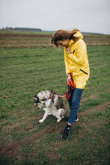 beautiful girl in a yellow raincoat on a green field. portrait of a woman in a yellow cloak with a husky dog. Love your dog and protect it from war.