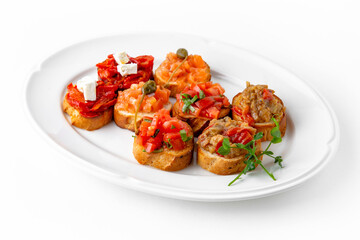 Mini bruschetta with salmon and capers, eggplant caviar, tomatoes and roasted peppers on a white plate