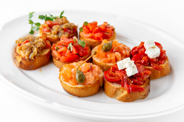 Mini bruschetta with salmon and capers, eggplant caviar, tomatoes and roasted peppers on a white...