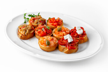Mini bruschetta with salmon and capers, eggplant caviar, tomatoes and roasted peppers on a white plate