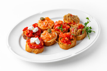 Mini bruschetta with salmon and capers, eggplant caviar, tomatoes and roasted peppers on a white plate