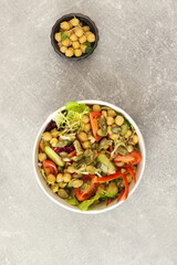 Vegetarian salad with chickpeas, tomatoes, cucumbers, bell peppers and pumpkin seeds in round paper container on  gray background. Healthy food, restaurant dish delivery. Top view. Free space for text