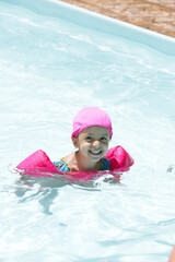 Fototapeta na wymiar Criança na piscina nadando com flutuador rosa com água azul.