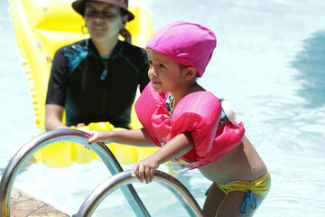 Criança na piscina nadando com flutuador rosa com água azul.