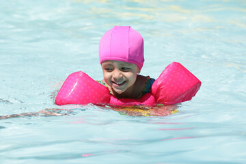 Criança na piscina nadando com flutuador rosa com água azul. © Luis Lima Jr