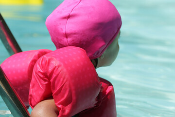 Criança na piscina nadando com flutuador rosa com água azul.