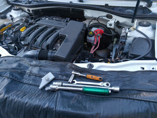 Car being repaired with the hood open and without its battery. Visible work tools