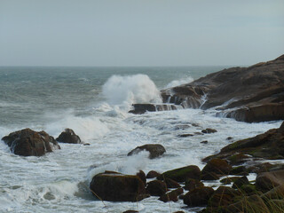 a wave-ridden area, with rocks covered with white foam and in the background the gray ocean...