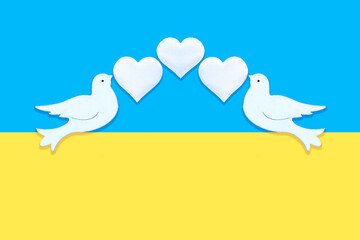 Two white figurines of a doves of peace with hearts in their beaks on the background of the colors...