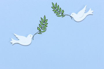 Two white figurines of a doves of peace with olive tree branch in their beaks on the light blue background. Peace Concept