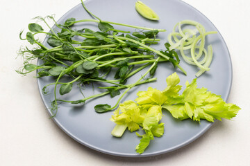 Pea sprouts and celery leaves on gray plate.