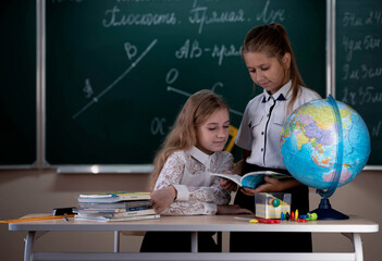 schoolgirls sit at the table in the classroom against the background of the blackboard