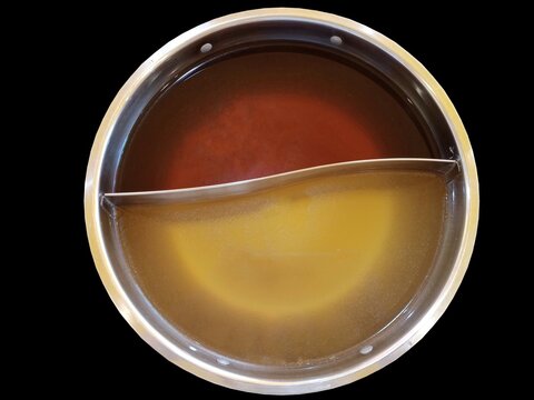 Shabu soup in the shaba pot consists of black water soup and clear soup base, divided in half isolated black background.