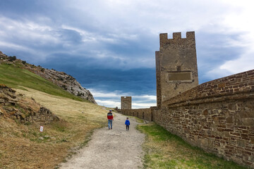 A man with a child against the background of an ancient Genoese fortress with a stormy sky, Sudak, Crimea, May 2021