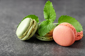 French pink and green macarons cookies with mint leaves on dark stone background