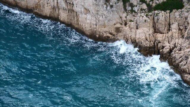 High angle view with waves of rough mediterranean sea breaking on the steep cliffs of mountain range Massif des Calanques near Cassis, French Riviera.