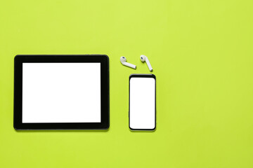 Tablet computer, mobile phone and earphones on green background