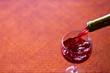 A selective focus shot of a glass of red wine on a table being poured from a bottle. The shot is composed to provide negative space for design possibilities