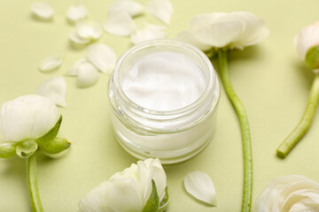 Jar of cosmetic product and ranunculus flowers on green background, closeup