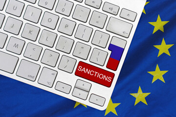 White computer keyboard with button of flag Russia and red button with word of sanctions on EU flag...