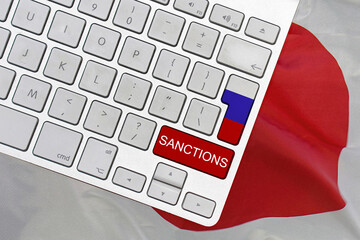 White computer keyboard with button of flag Russia and red button with word of sanctions on Japan...