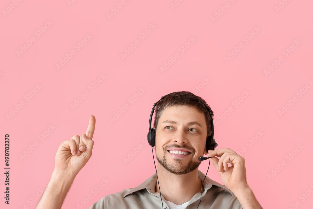 Poster smiling consultant of call center in headset pointing at something on pink background