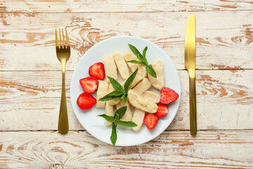 Plate with tasty lazy dumplings, strawberry, mint and cutlery on light wooden background