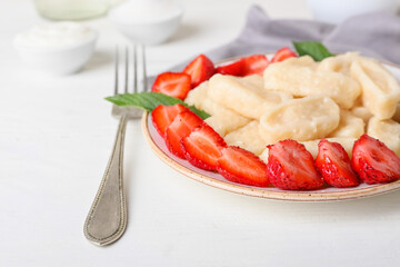 Plate with delicious lazy dumplings, ripe strawberry and fork on light wooden background, closeup