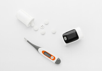 Pulse oximeter, thermometer and pills on white background