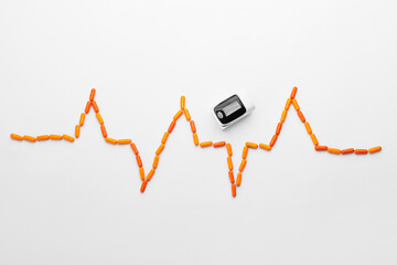 Cardiogram made of orange pills and pulse oximeter on white background