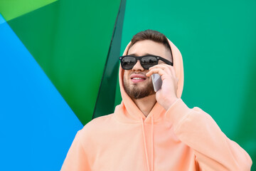 Young guy in stylish hoodie talking by phone outdoors