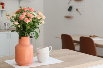 Beige vase with beautiful roses and cups on counter in kitchen