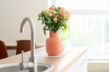 Beige vase with beautiful roses on counter in kitchen