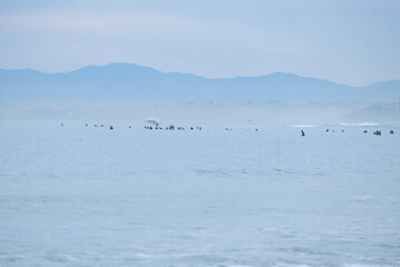 Surfers wait on the waves with mountains in background