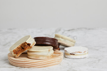 Argentinian white and dark chocolate aljafores with dulce de leche on a wooden plate on a marble table.