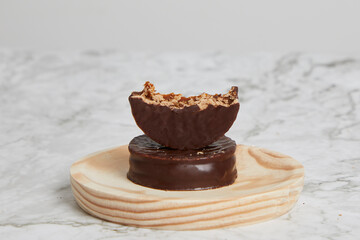 Argentinean dark chocolate alfajores with dulce de leche on a wooden plate on a marble table.