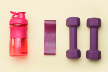Stylish dumbbells, elastic band and bottle on yellow background