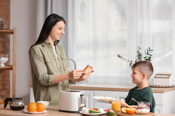 Little boy with his mother putting toasted bread slices onto plate in kitchen