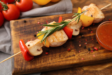 Board of grilled chicken skewers with vegetables and sauce on wooden background, closeup
