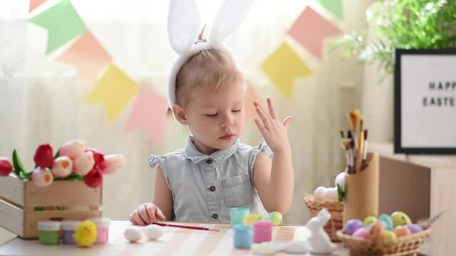 A two-year-old girl in bunny ears draws Easter eggs. happy Easter. Do it yourself