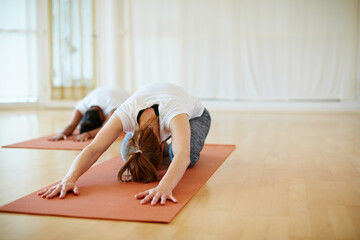 Stretching away the stress. Shot of two women doing yoga together in a studio.