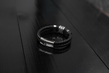 Black leather male bracelet with metal pendant on the dark wooden desk