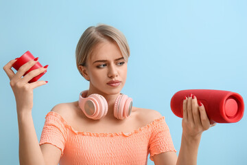 Woman with modern headphones choosing wireless portable speaker on blue background