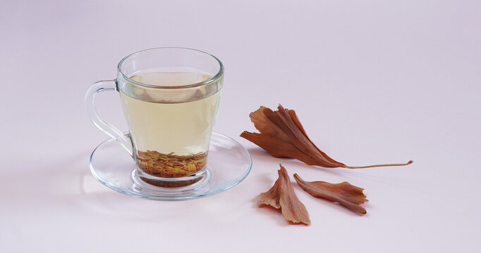 Glass Cup Of Tea On Light Pink Background With Dried Yellow Gingko Biloba Leaves. Copy Space. Top View