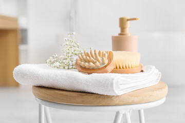 Body massage brushes, gypsophila flowers, bottle with cosmetic product and towel on table in bathroom